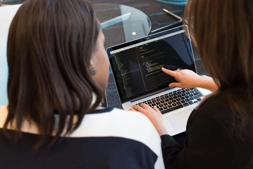 Zwei Frauen vor einem Laptop mit Programmiercode