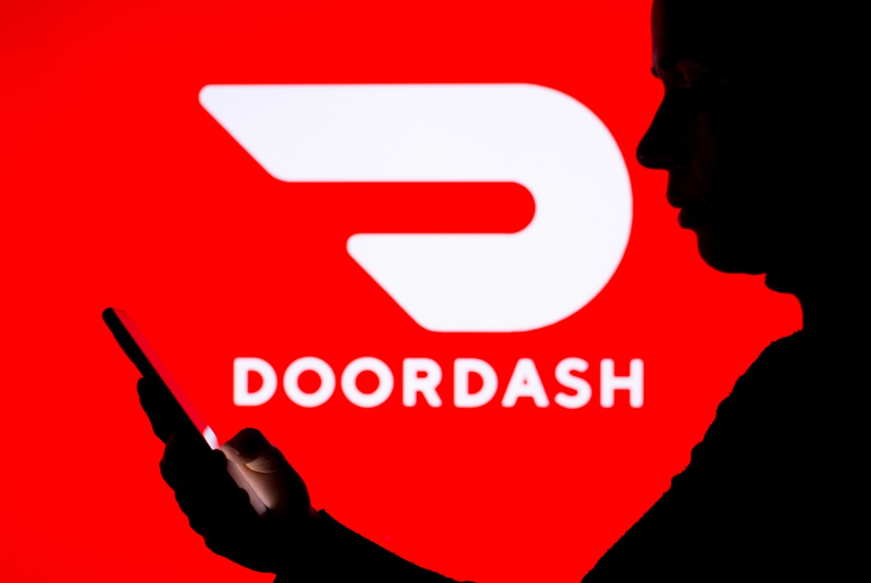 DoorDash Logo hinter einem Mann mit Smartphone