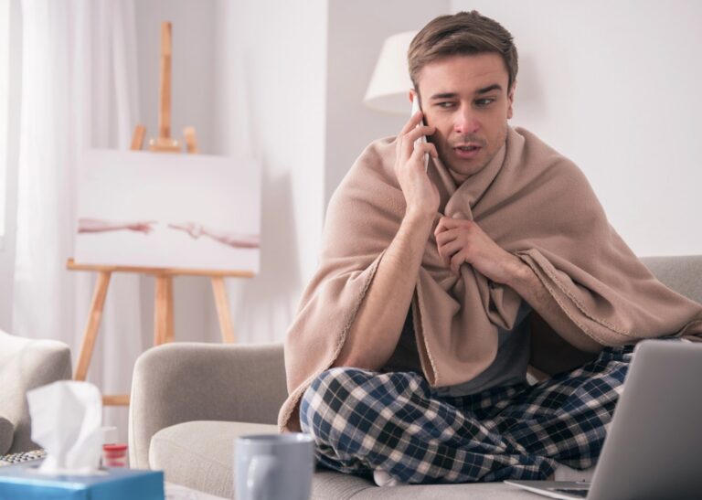 Erkaelteter Mann mit Decke und Smartphone