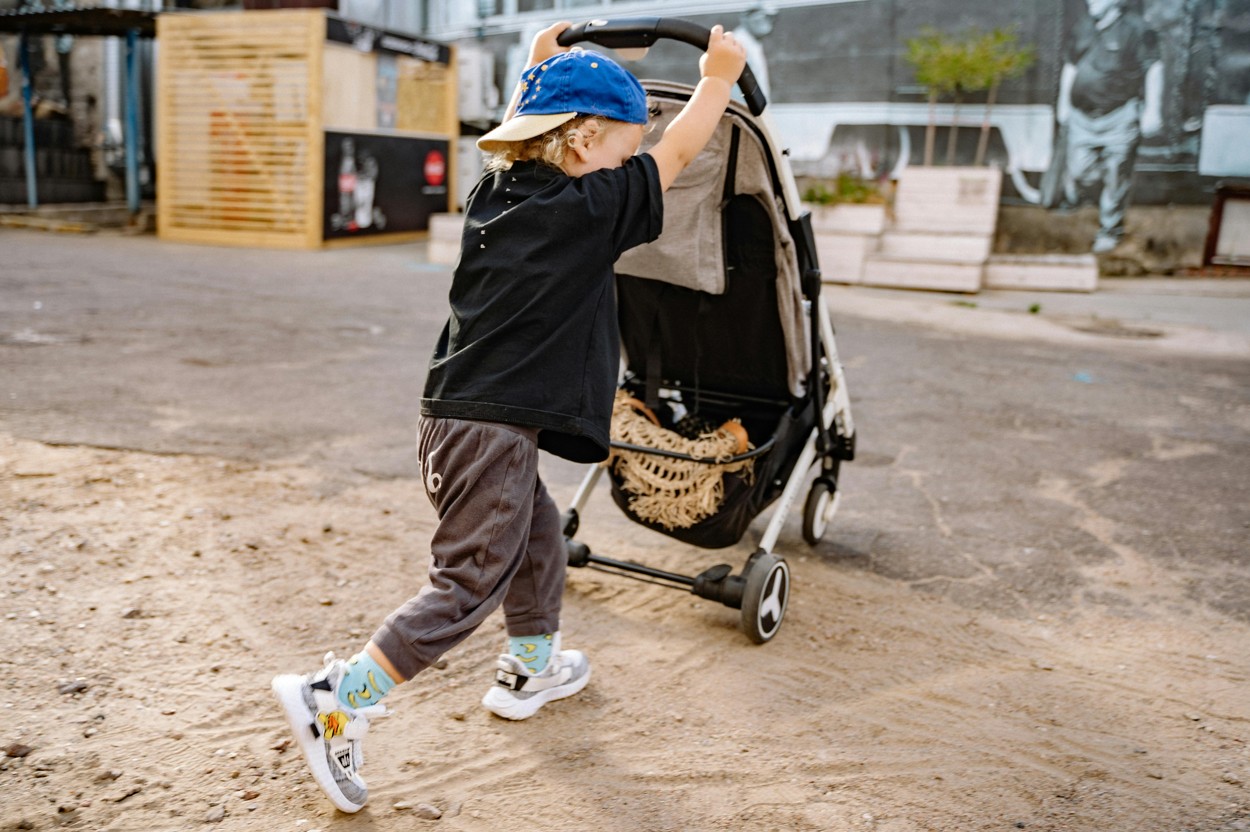 Junge mit Kinderwagen auf Sandflaeche