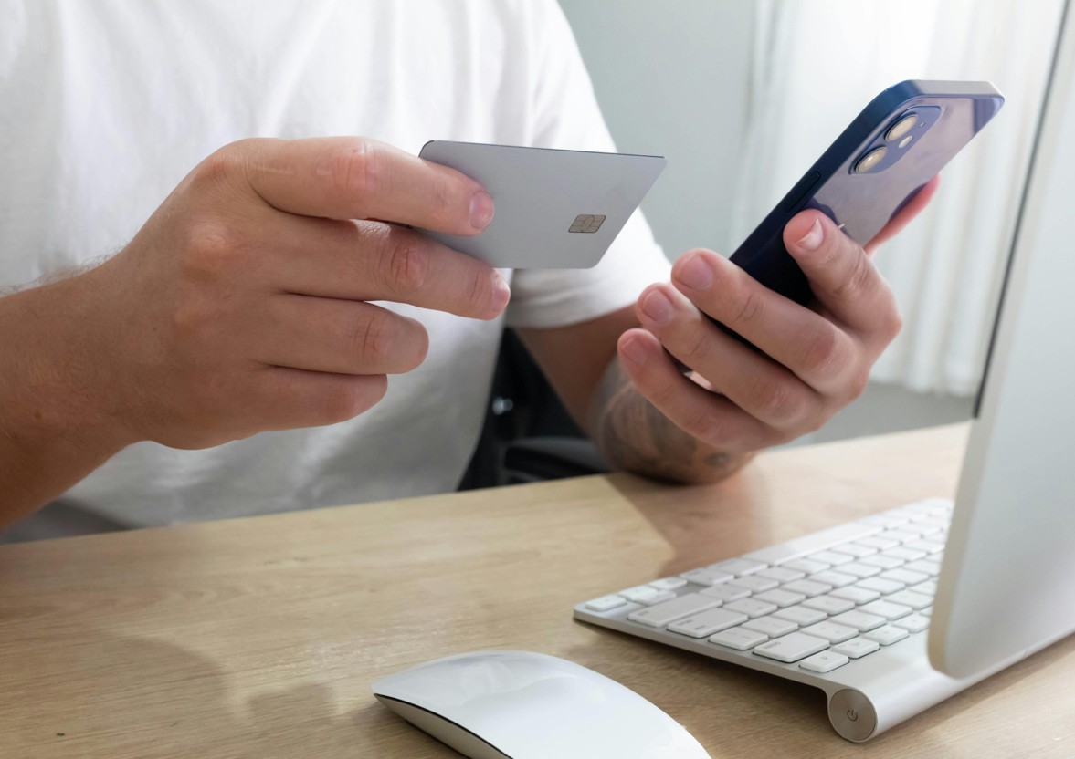 Mann mit Kreditkarte und Smartphone vor Macbook