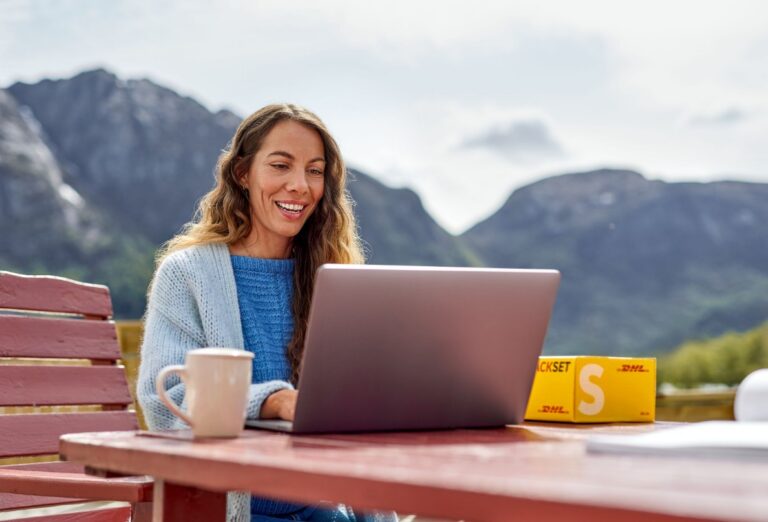 Frau mit Laptop und DHL Paket auf einem Gartentisch