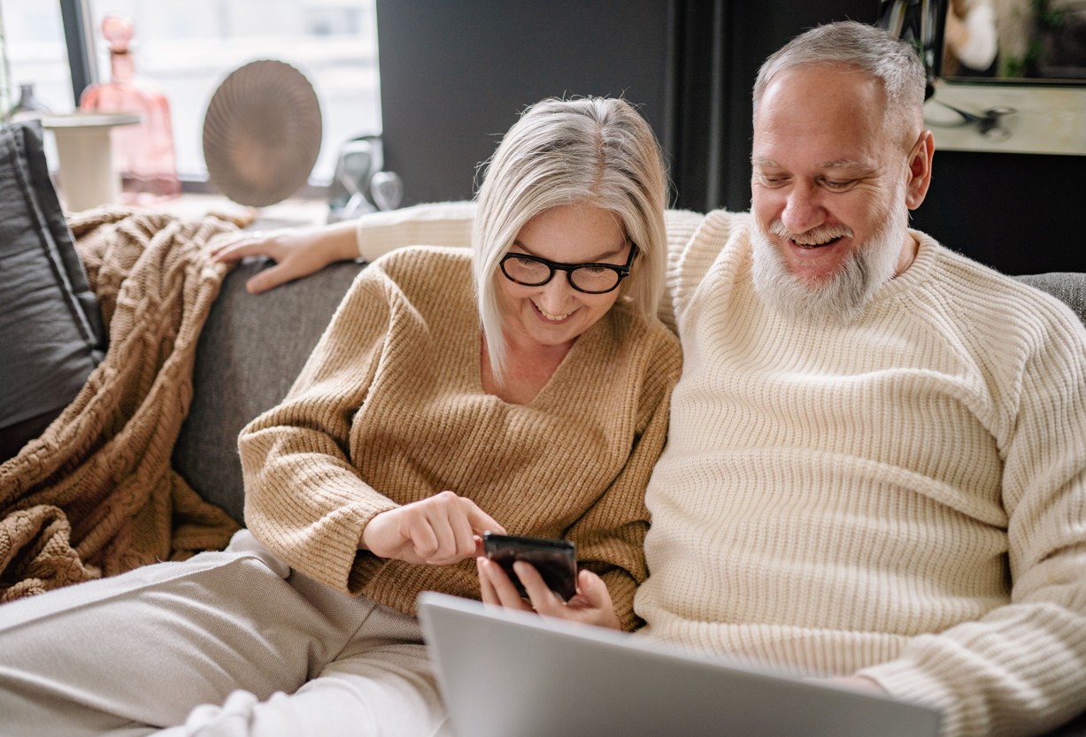 Aelteres Paar auf der Couch mit Laptop und Smartphone