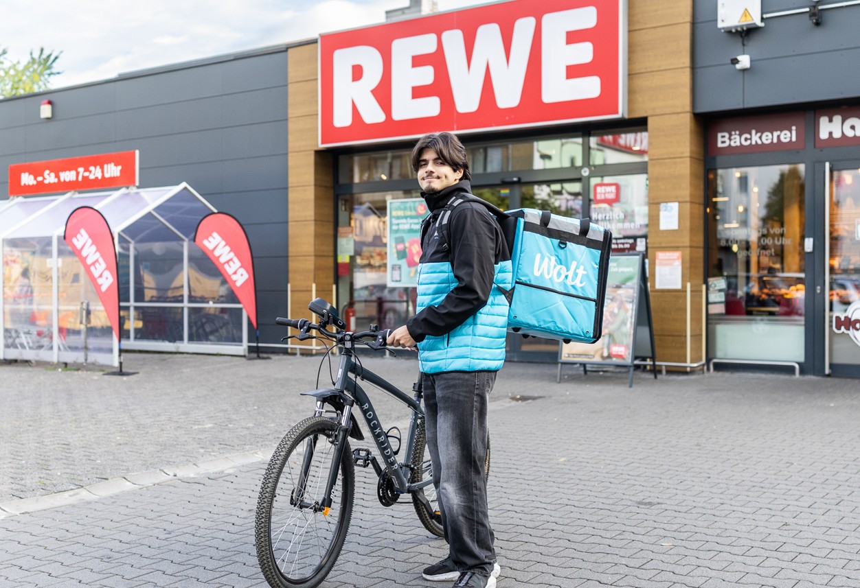 WOLT Rider vor einem REWE Markt
