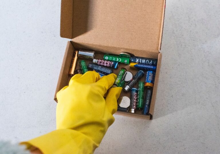 Hand mit Gummihandschuh und Box mit Batterien
