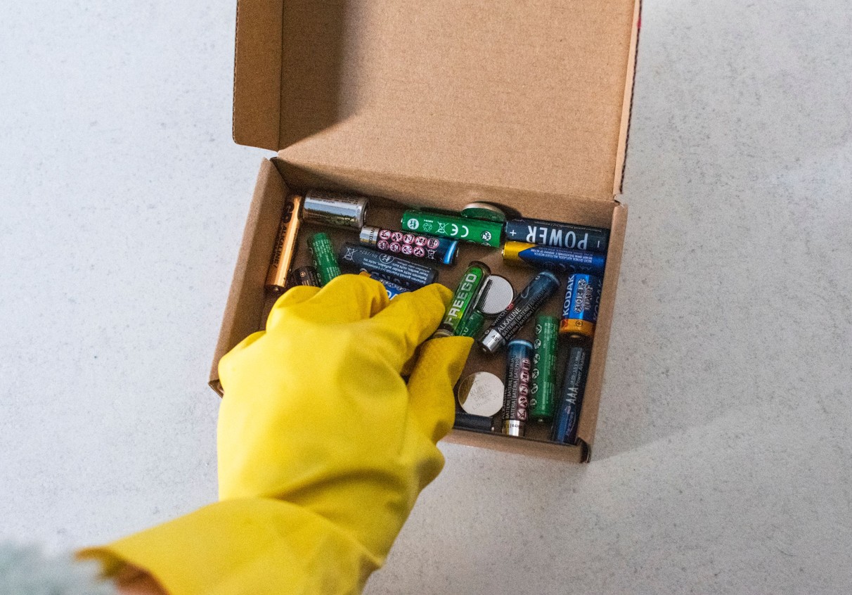 Hand mit Gummihandschuh und Box mit Batterien