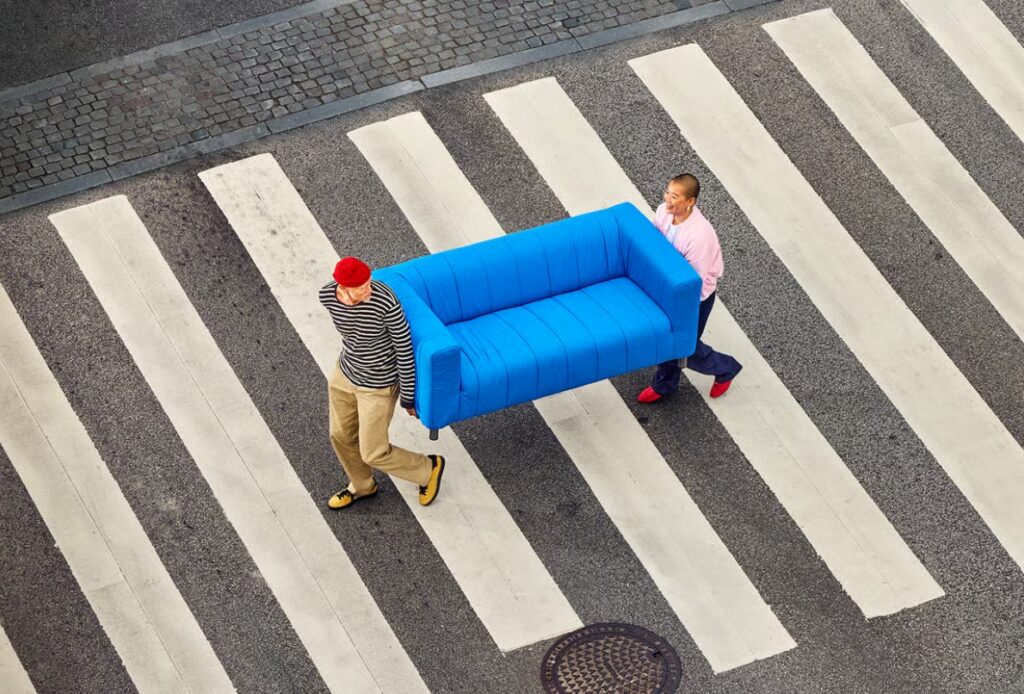 Zwei Maenner tragen ein blaubes IKEA Sofa